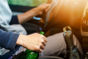 man holding alcohol bottle drinking alcohol while driving a car