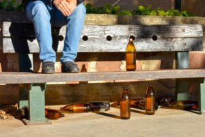 man sat on a bench with many big orange bottles of beer made of glass completely empty at the park due to somebody has drunk