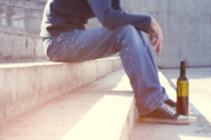 Man depressed with wine bottle sitting on stairs outdoor. People abuse and alcoholism problems