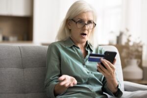 Shocked woman holding card and smartphone, experiencing failed transaction while purchasing online