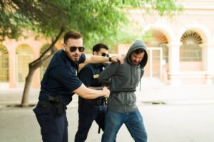 Angry caucasian man making eye contact while beating a criminal with a baton after an arrest