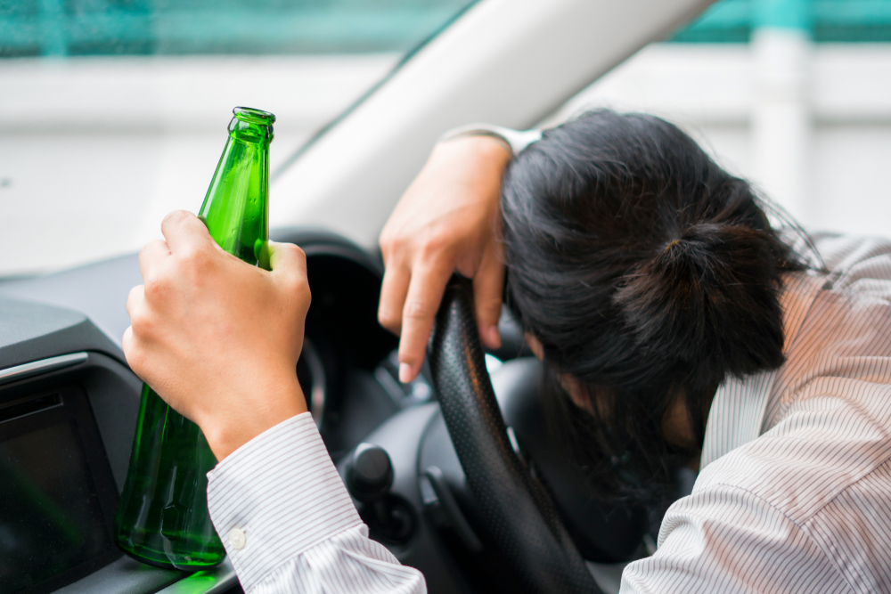 Drunk young man driving a car with a bottle of beer.